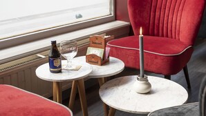 A modern interior with a red chair, a table with a candle, and a bottle of beer. - Beverly Hills Hotel (Brussels)