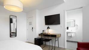 A modern hotel room with a bed, desk, chair, TV, and a red armchair. - Beverly Hills Hotel (Brussels)