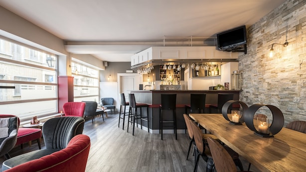 A modern kitchen with a bar area, wooden flooring, and a stone accent wall. - Beverly Hills Hotel (Brussels)