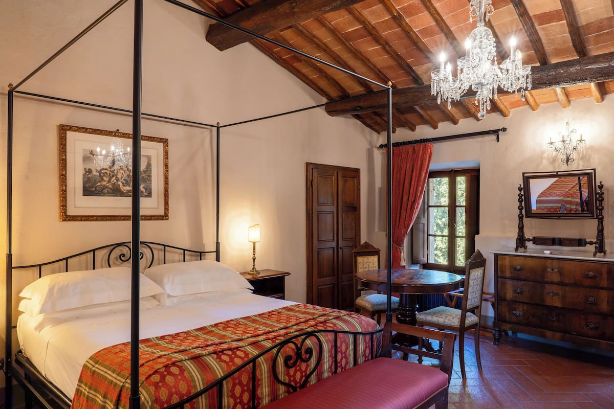 A four-poster bed with a canopy, a wooden dresser, a chandelier, and a framed picture on the wall.