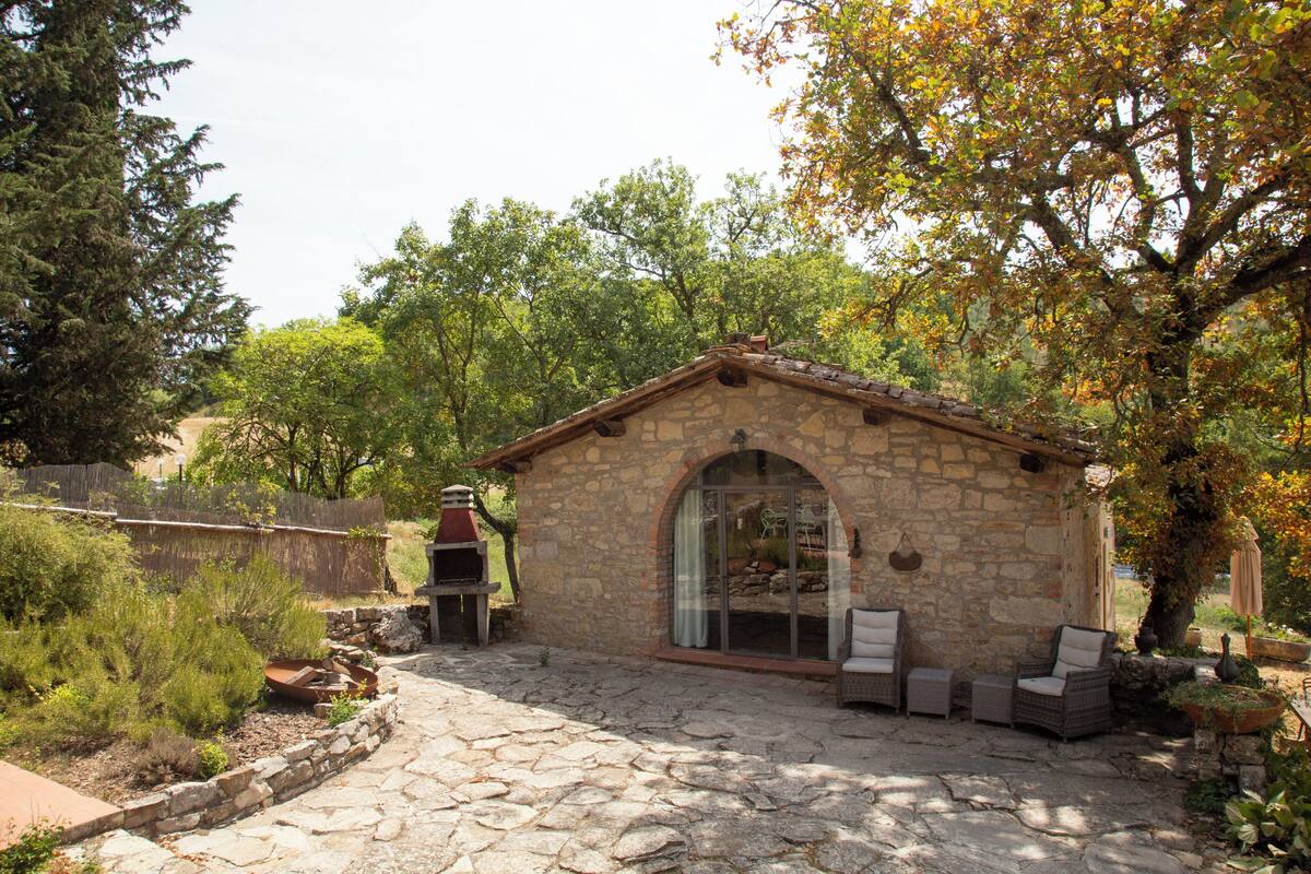 A stone building with a tiled roof, a glass door, and a patio area with outdoor furniture.