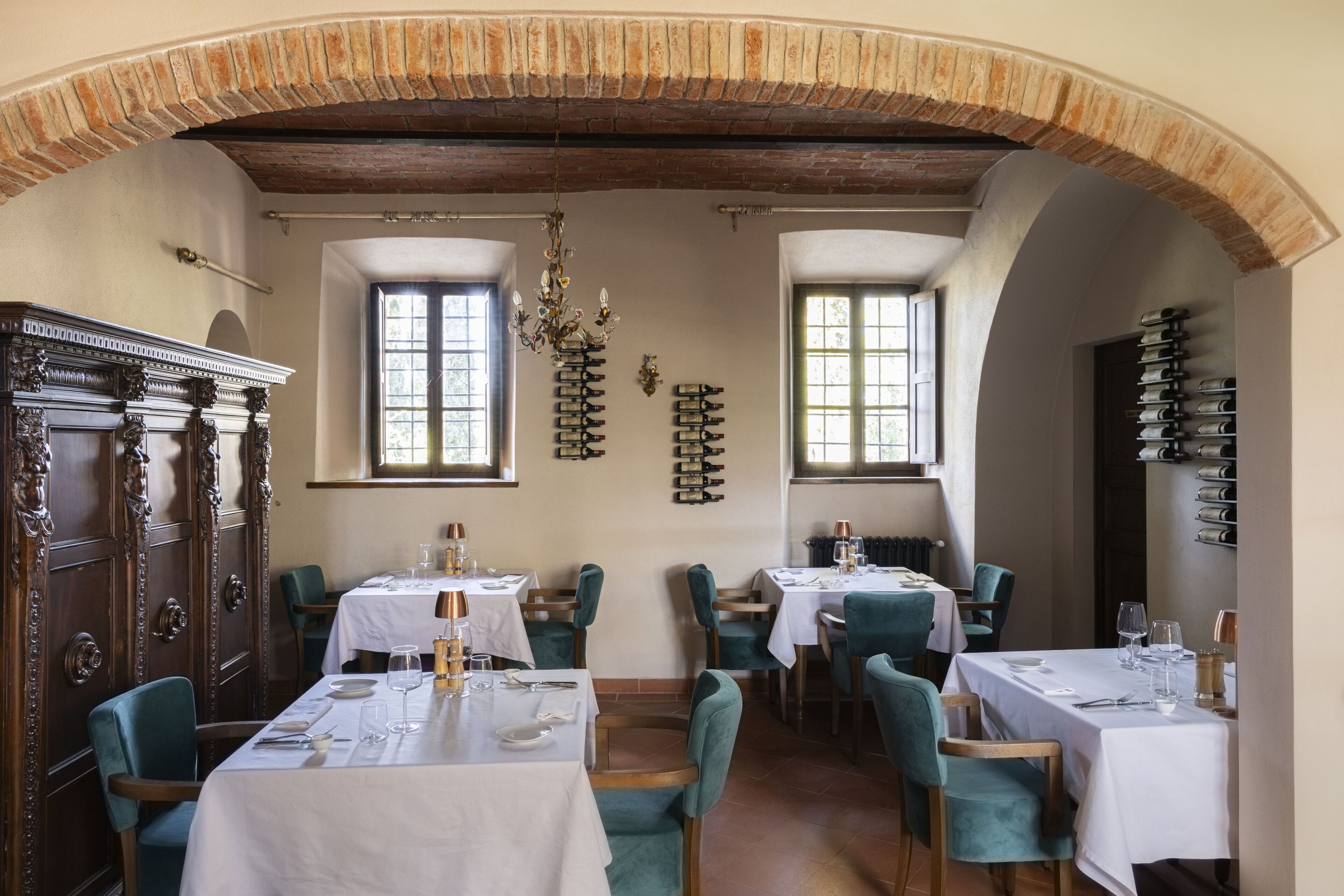 A restaurant with tables set for dining, a brick archway, and a chandelier.