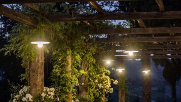 Una pergola in legno con tavoli e sedie sotto, circondata da piante e fiori.