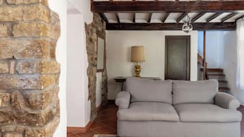 A living room with a stone wall, a grey sofa, a patterned rug, and a lamp on a small table.