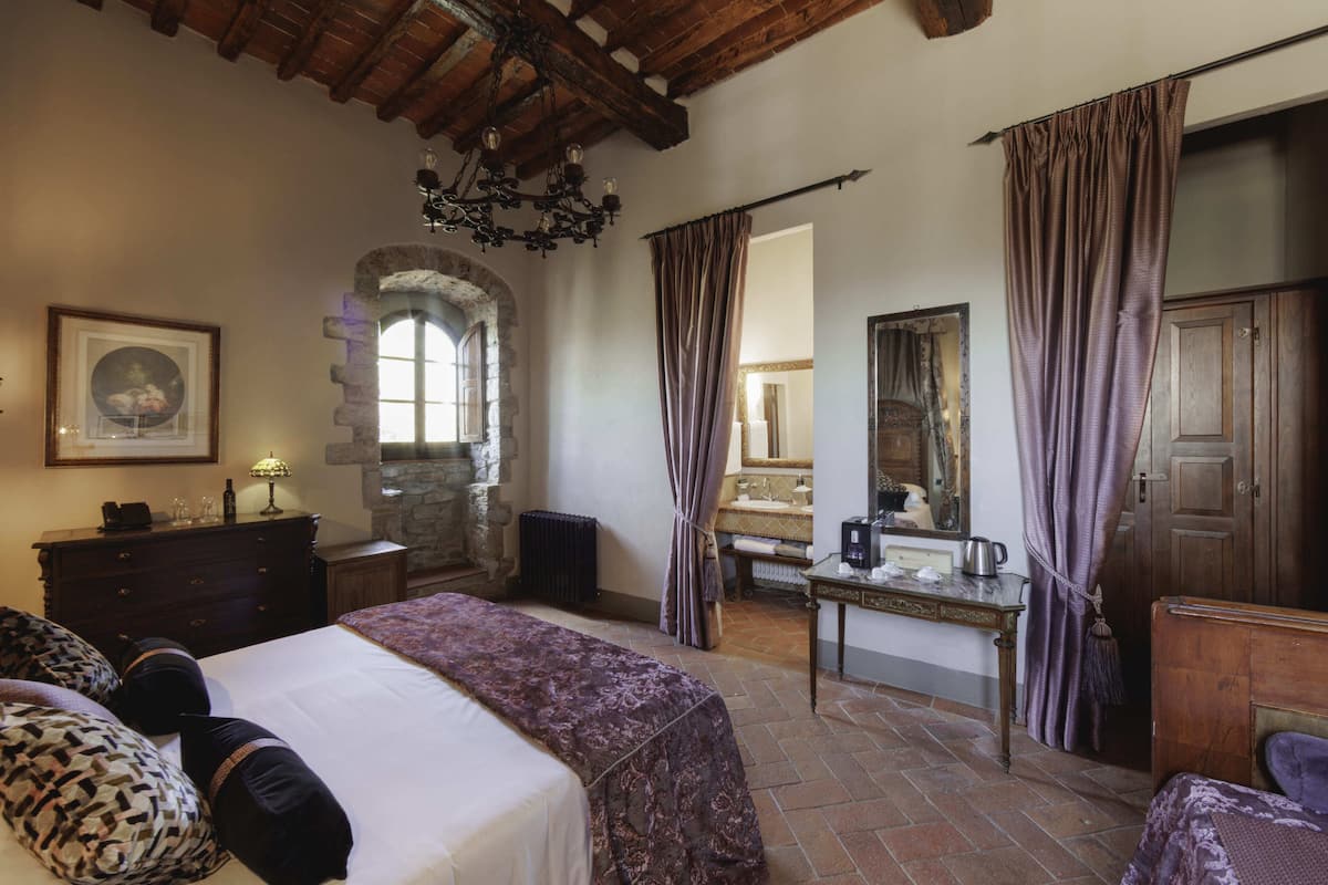 A room with a bed, a dresser, a desk, a mirror, and a stone archway.