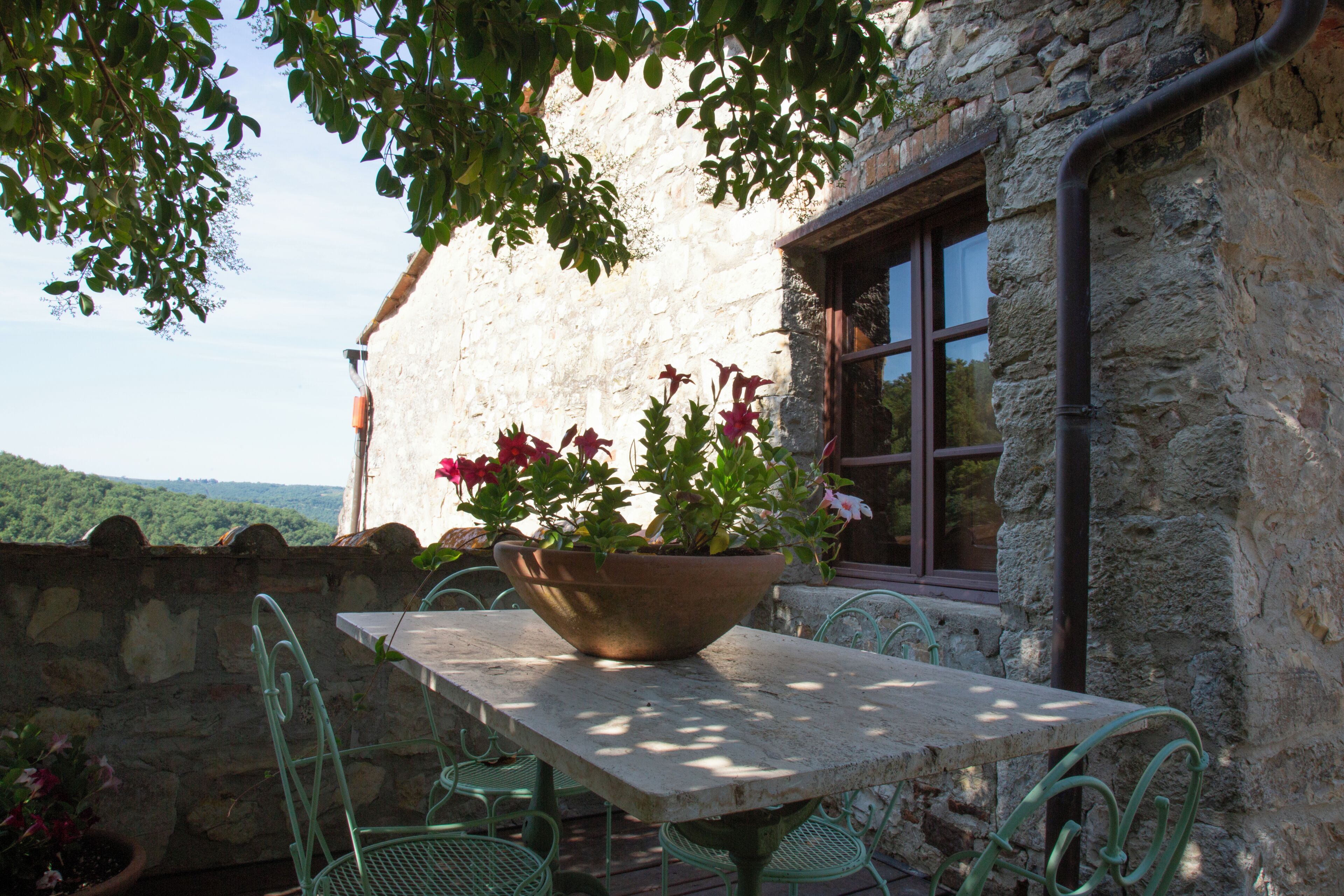 A stone building with a table and chairs, a window, and a view of the landscape.