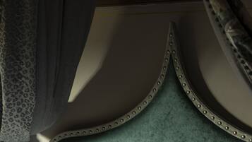 A bed with a green upholstered headboard, white pillows, and a canopy with a patterned curtain.