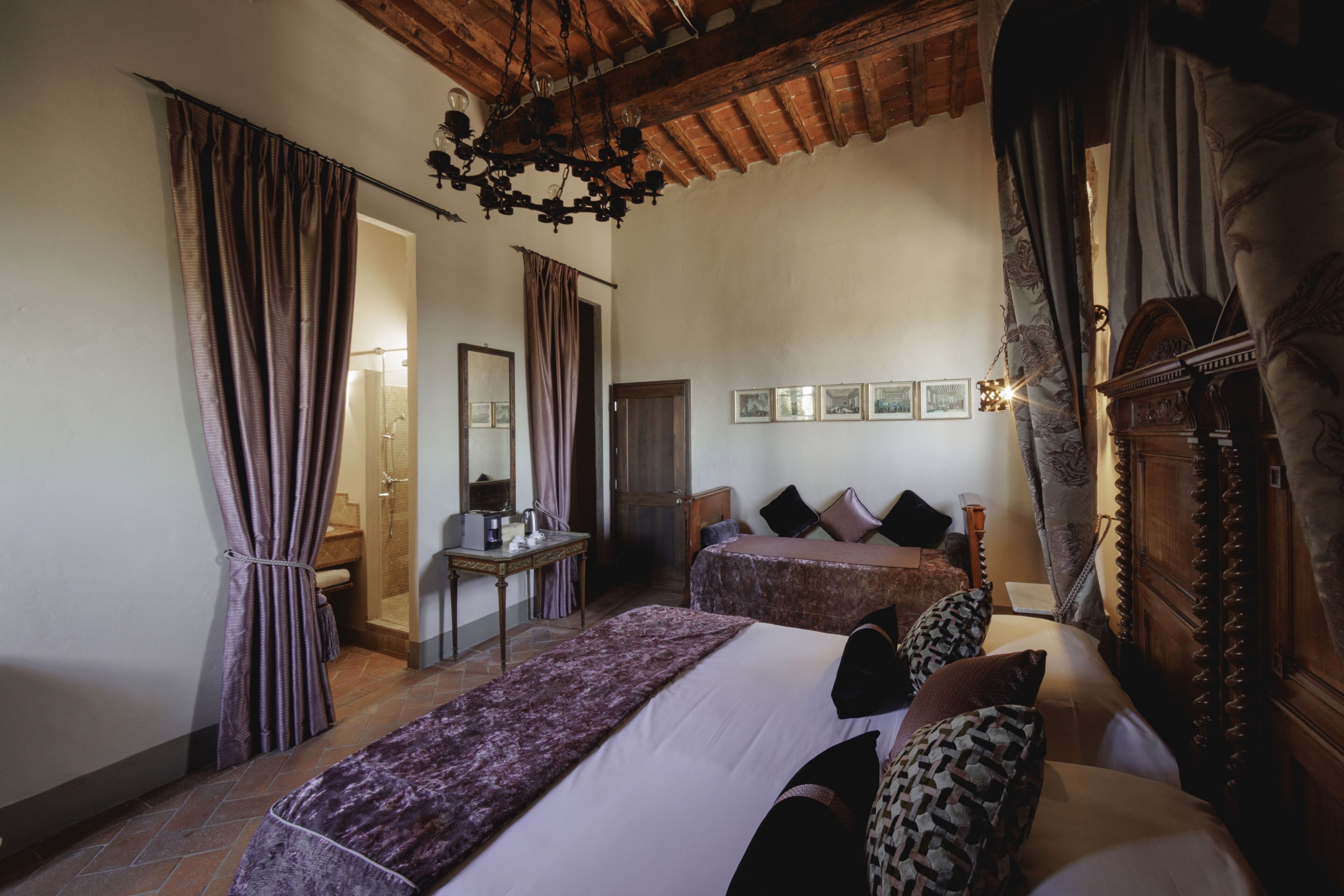 A bedroom with two beds, a wooden wardrobe, a desk with a chair, and a chandelier.