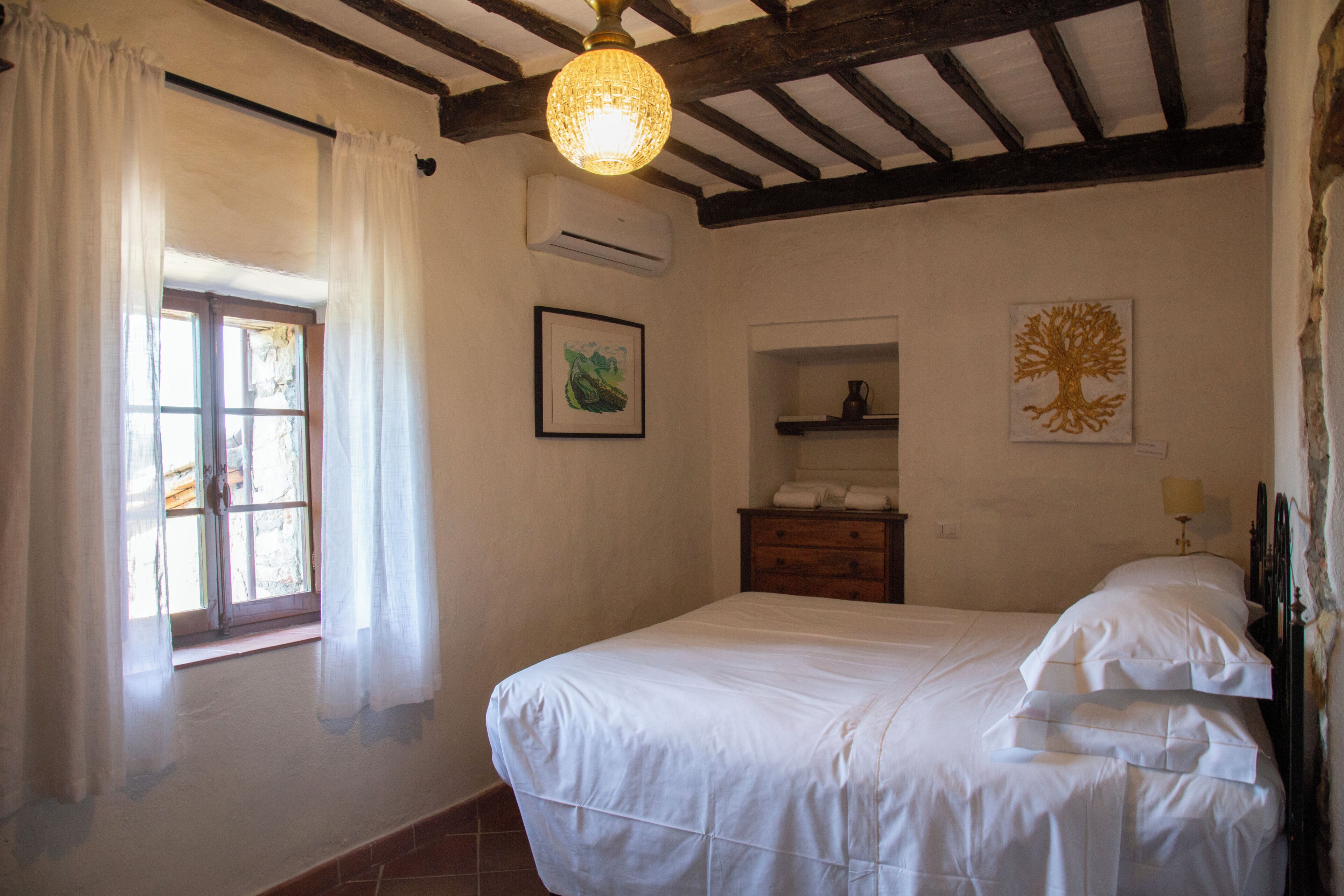 Un dormitorio con cama, ventana con cortinas, aire acondicionado, cómoda y estante montado en la pared.