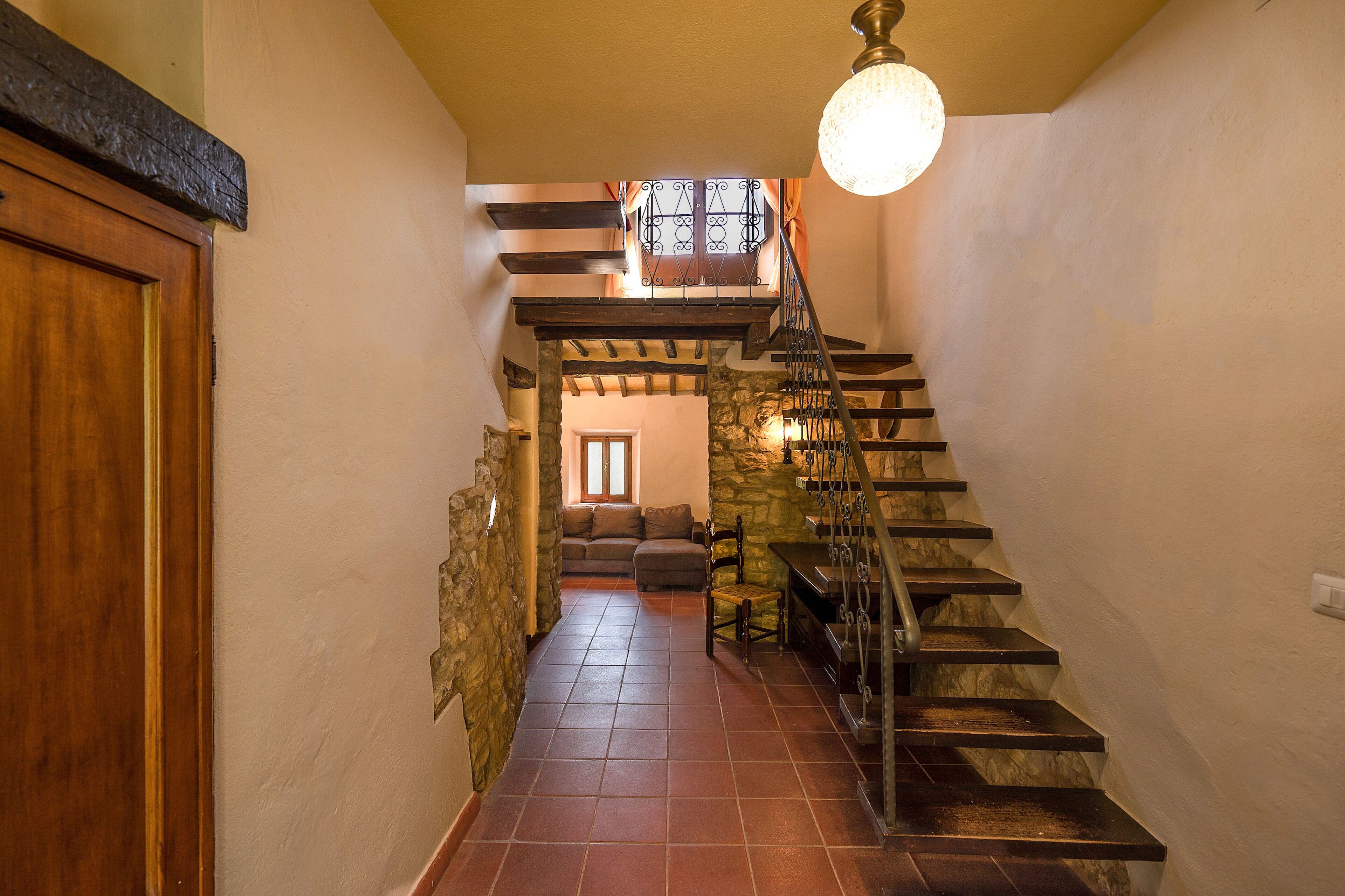 A staircase leading to a living area with a stone wall, a wooden door, and a hanging light fixture.
