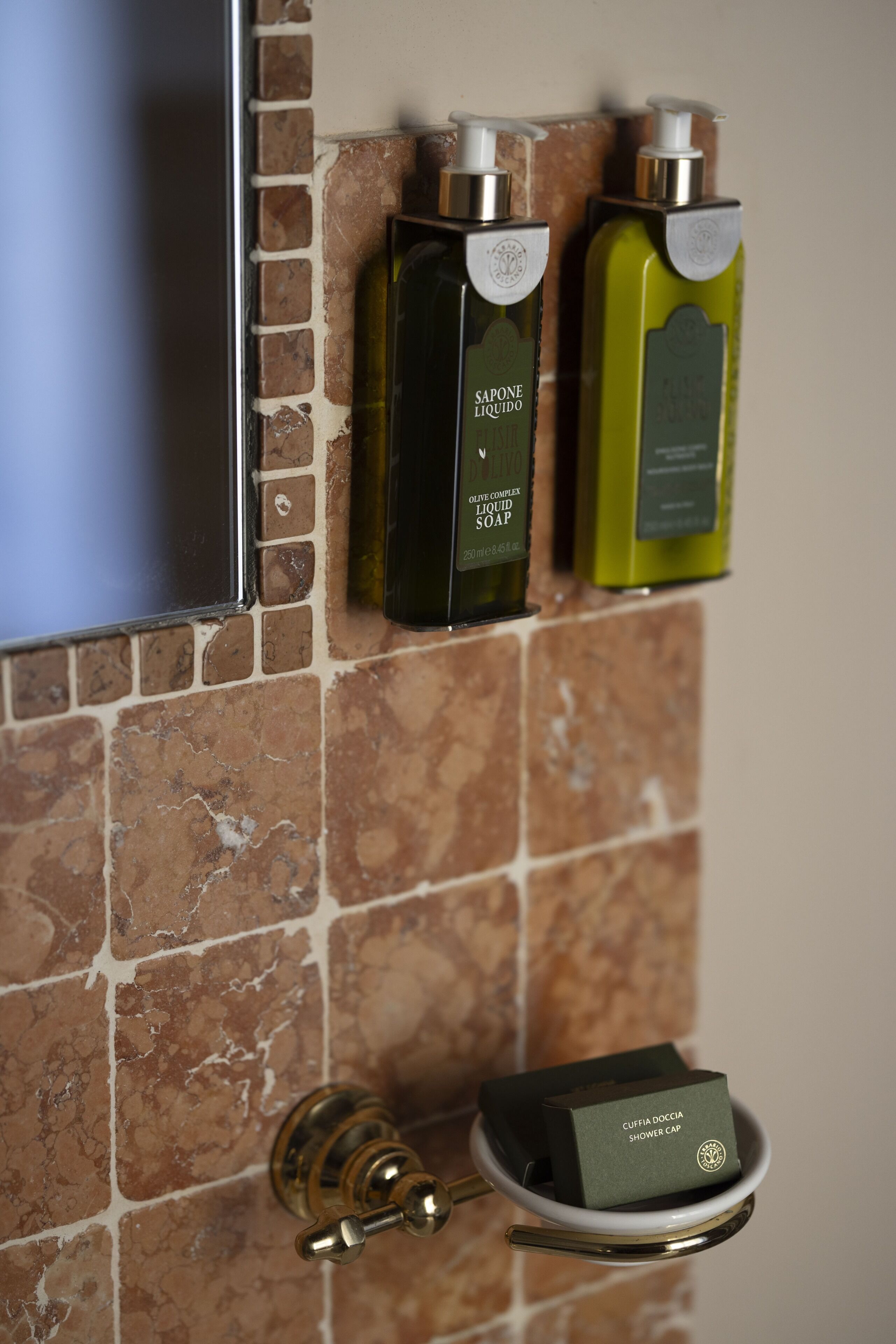 Une salle de bain avec un mur recouvert de carreaux, un téléviseur fixé au mur et deux bouteilles de savon liquide.