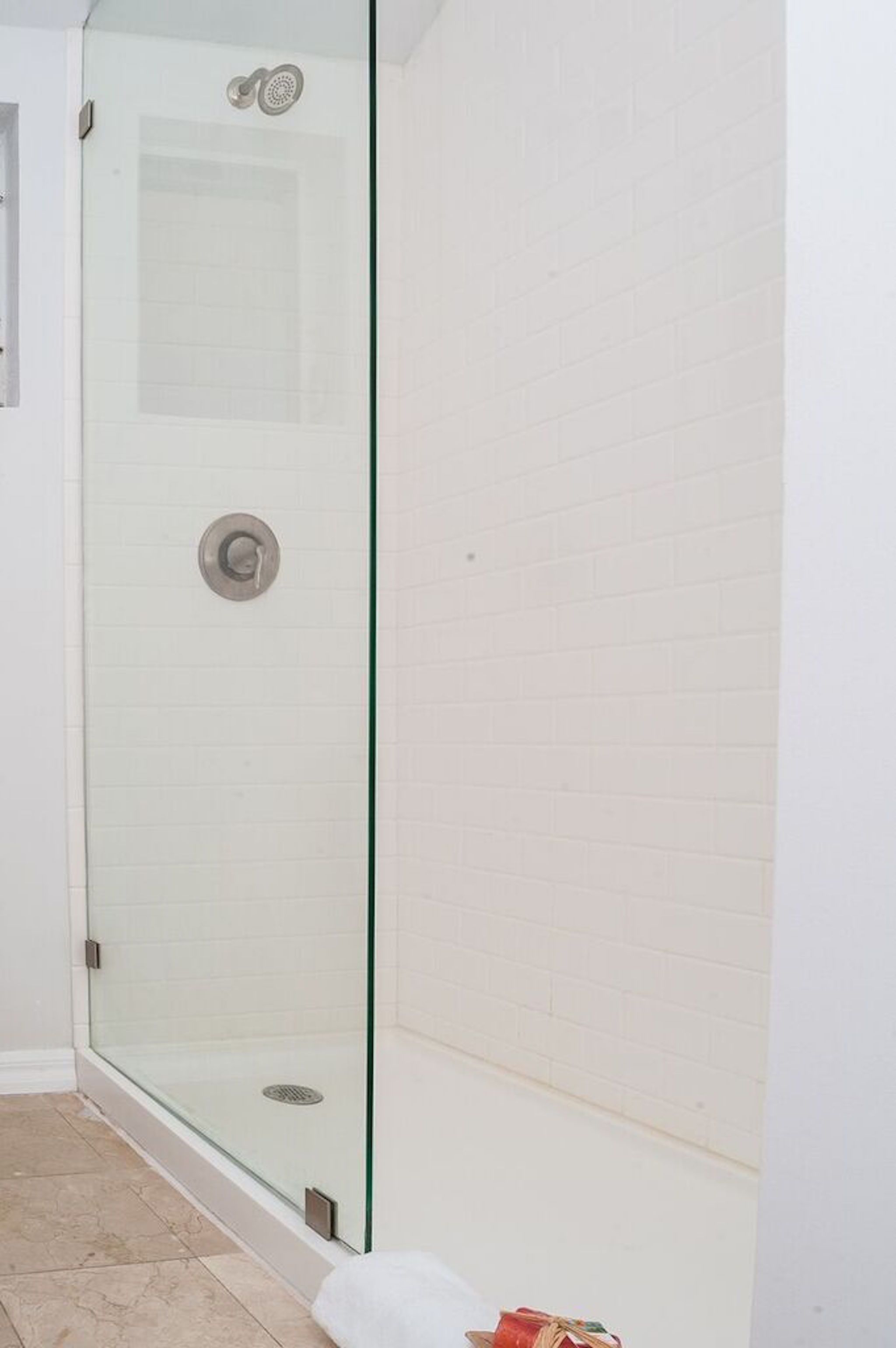 A glass-enclosed shower with a tiled floor and a white brick wall.