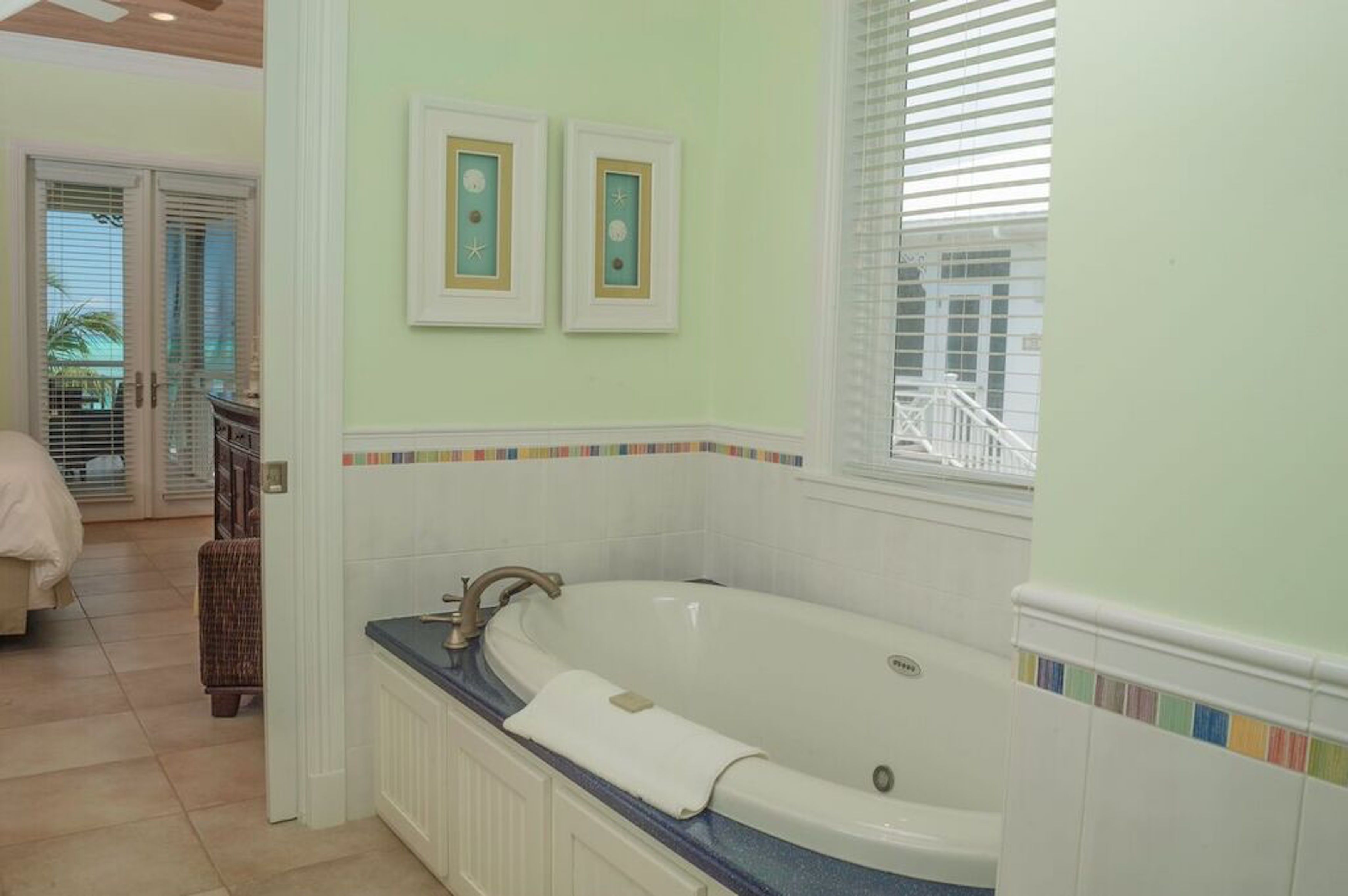 A bathroom with a large bathtub, a window with blinds, and a door leading to another room.