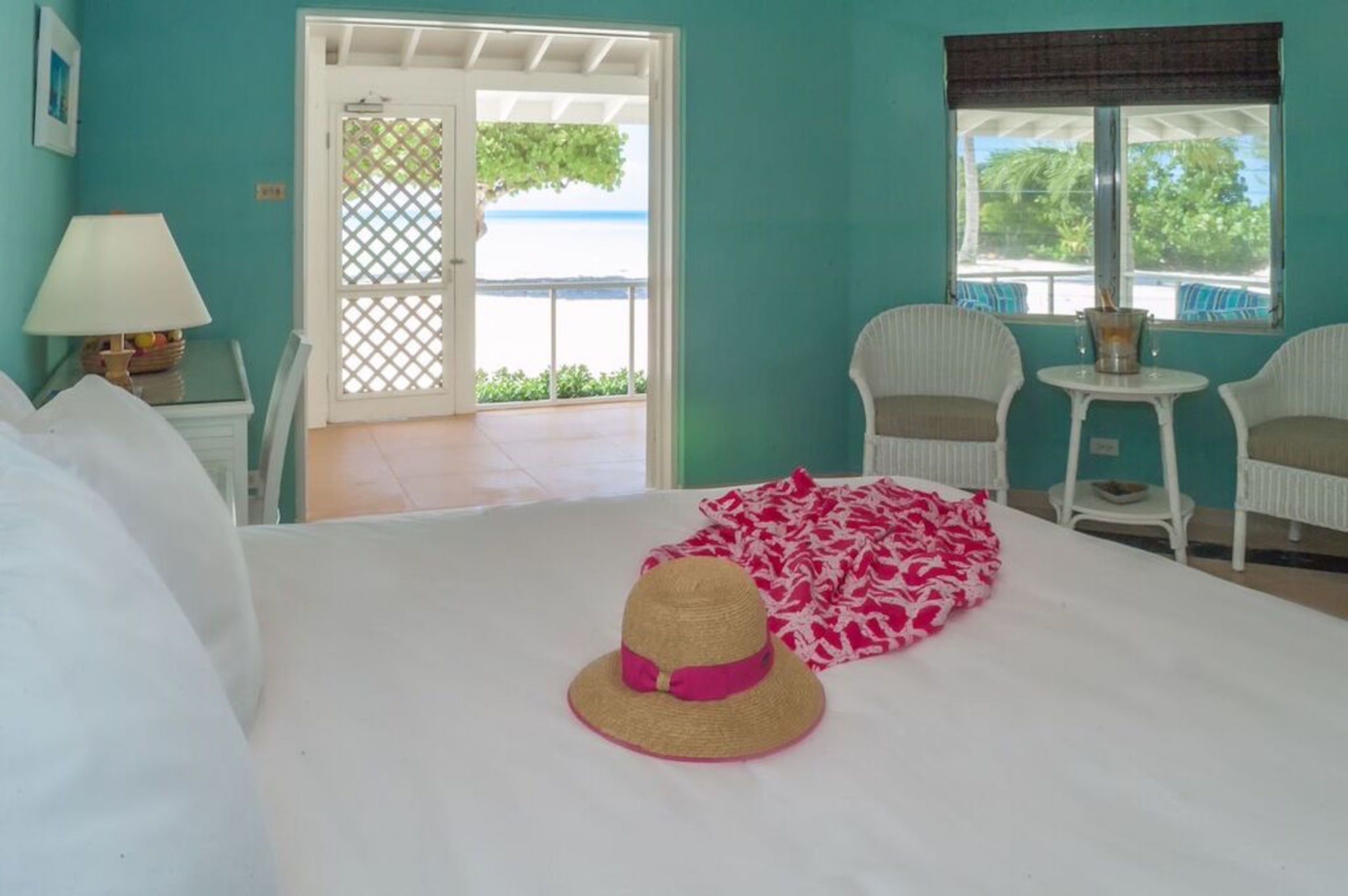 Une pièce avec un lit, un chapeau, une table avec des chaises et une vue sur la mer par une fenêtre.