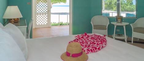 Une pièce avec un lit, un chapeau, une table avec des chaises et une vue sur la mer par une fenêtre.