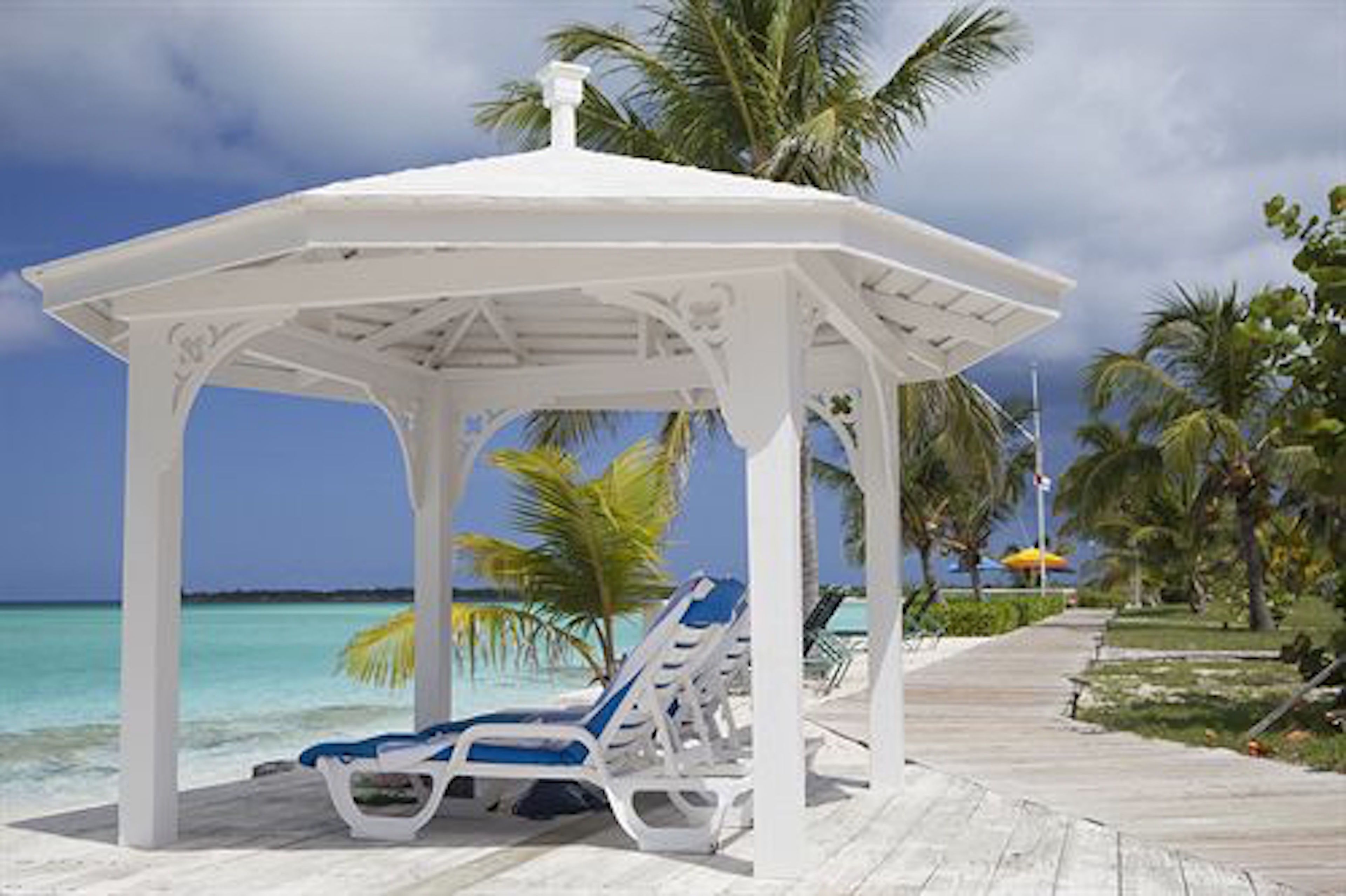A white gazebo with blue lounge chairs, a wooden deck, and a view of the ocean.