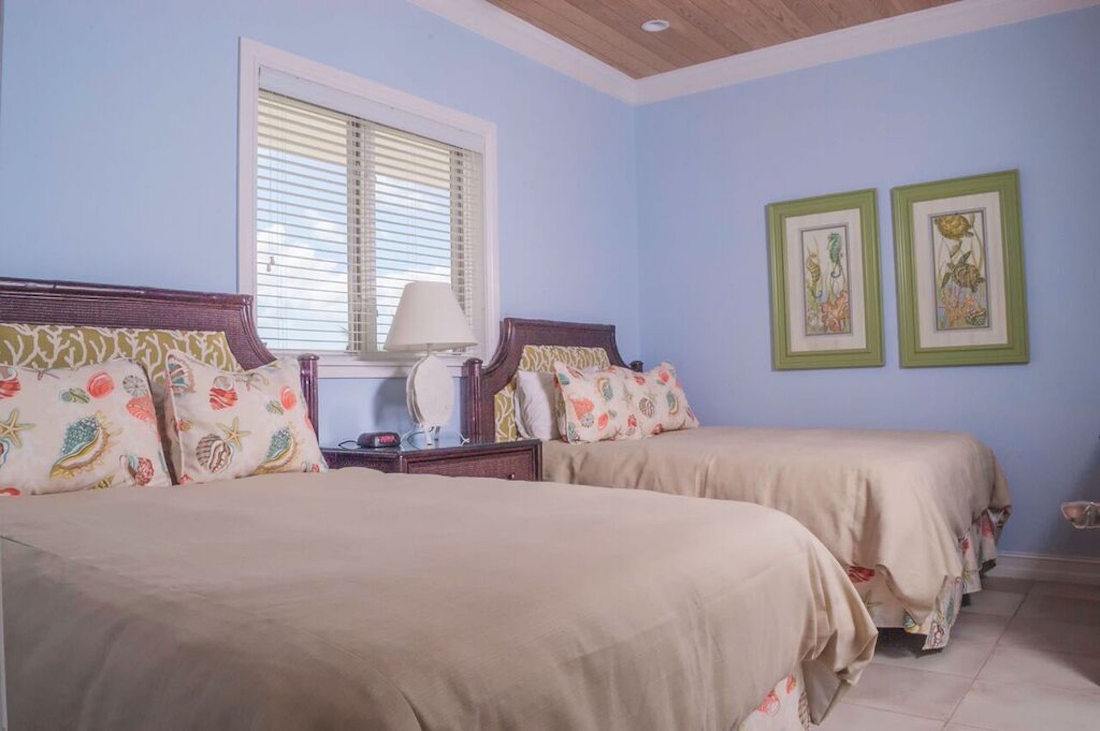 A bedroom with two beds, a nightstand, a lamp, and two framed pictures on the wall.
