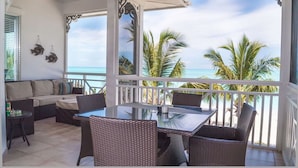 A balcony with a glass table and wicker chairs, overlooking a beach with palm trees and the ocean. - Cape Santa Maria Beach Resort (Galliot Cay)