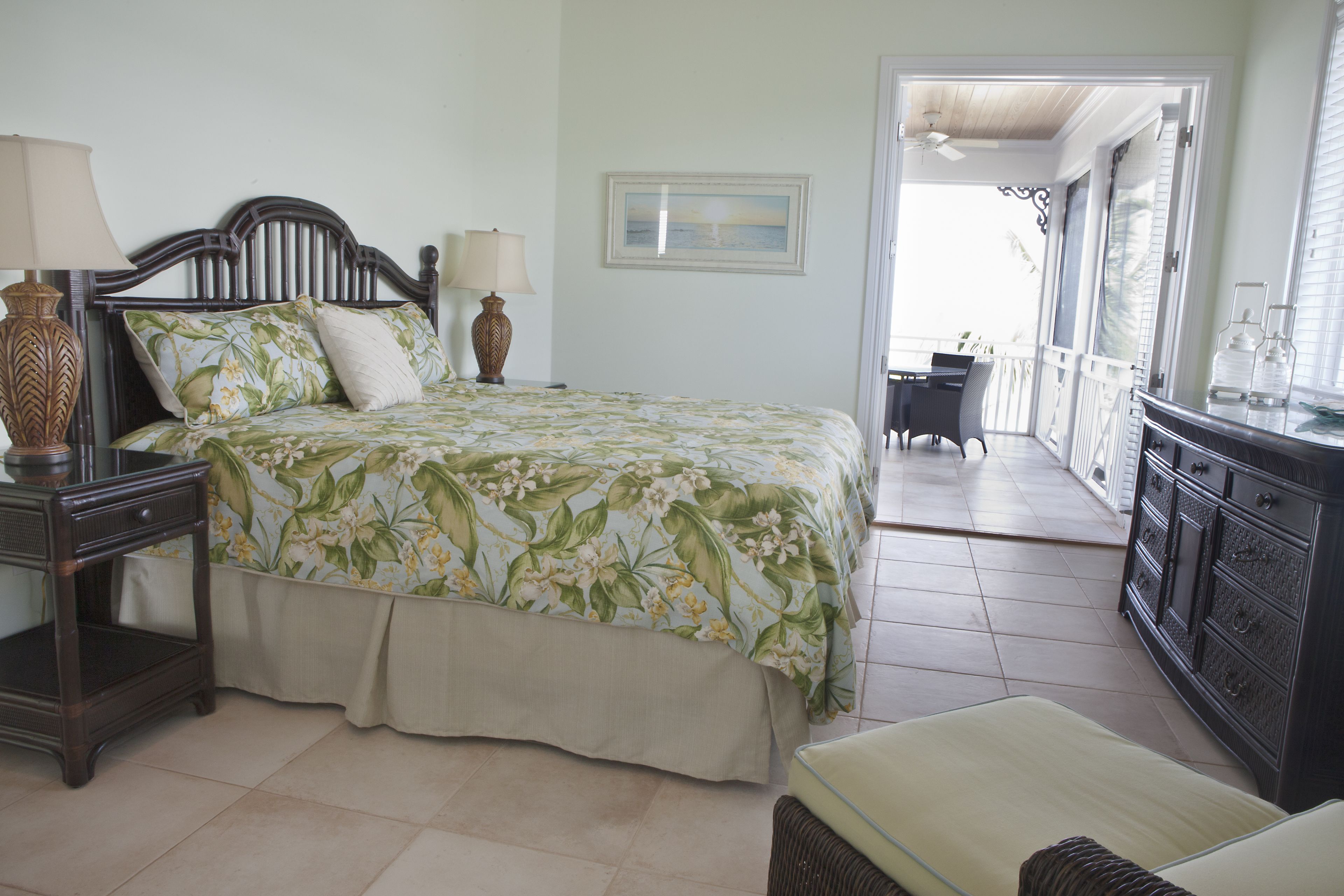 A bedroom with a bed, bedside tables, a dresser, and a balcony with a table and chairs.
