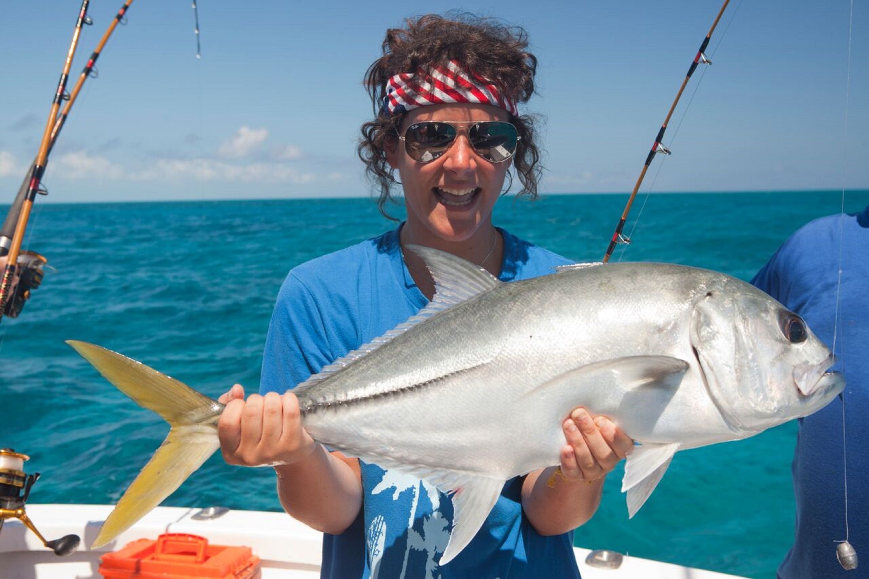 A person holding a large fish on a boat with fishing rods in the background.