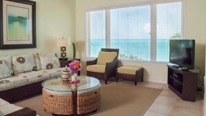 A living room with a sofa, armchairs, a glass coffee table, a TV, and a window with blinds. - Cape Santa Maria Beach Resort (Galliot Cay)