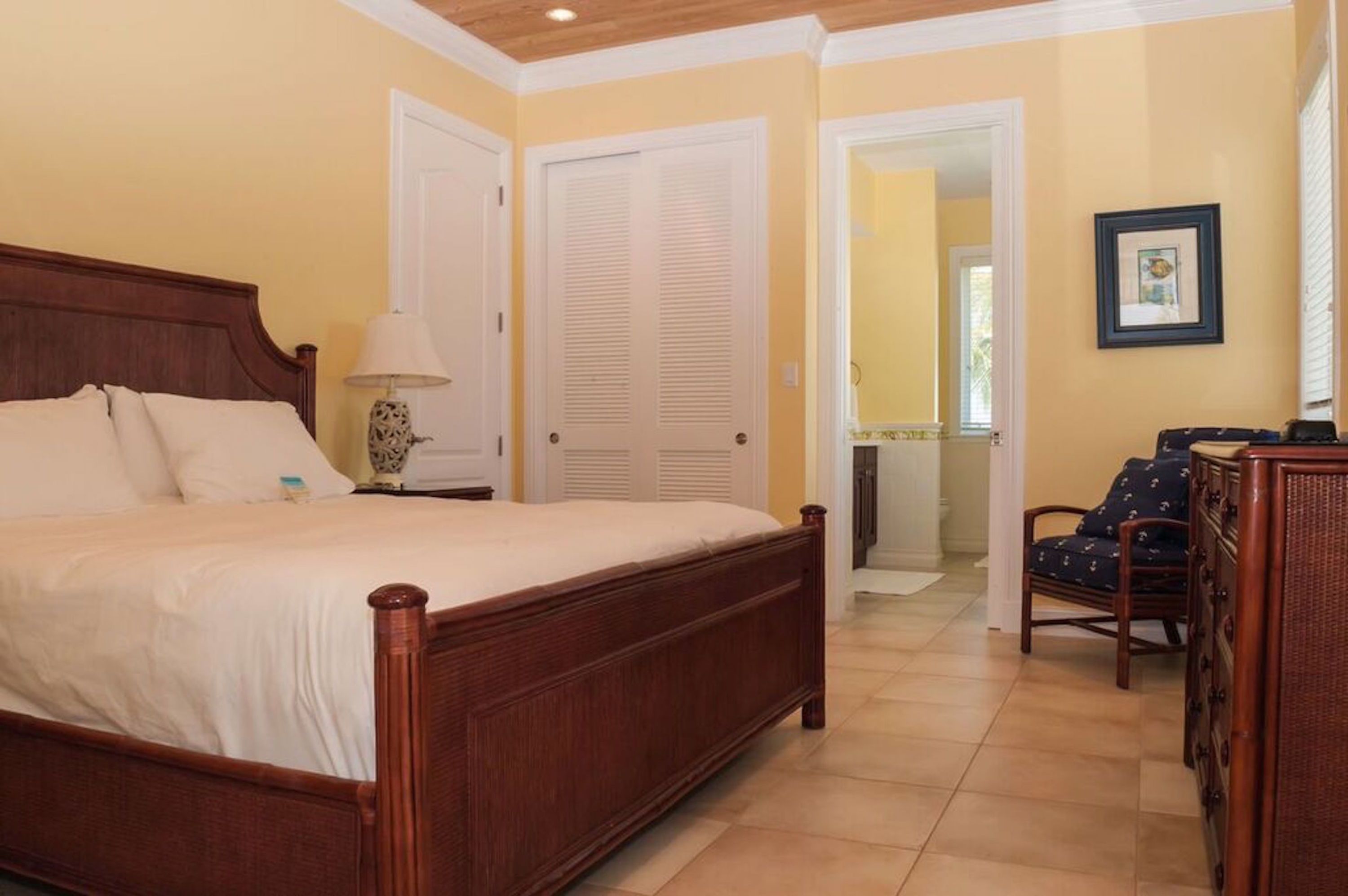 A bedroom with a wooden bed, white curtains, a bedside lamp, and a chair.