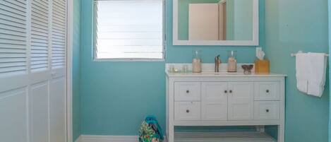 Une salle de bain avec un meuble-lavabo blanc, un miroir et une fenêtre avec des stores.