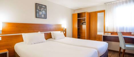 A hotel room with two beds, a desk, a chair, and a wardrobe.