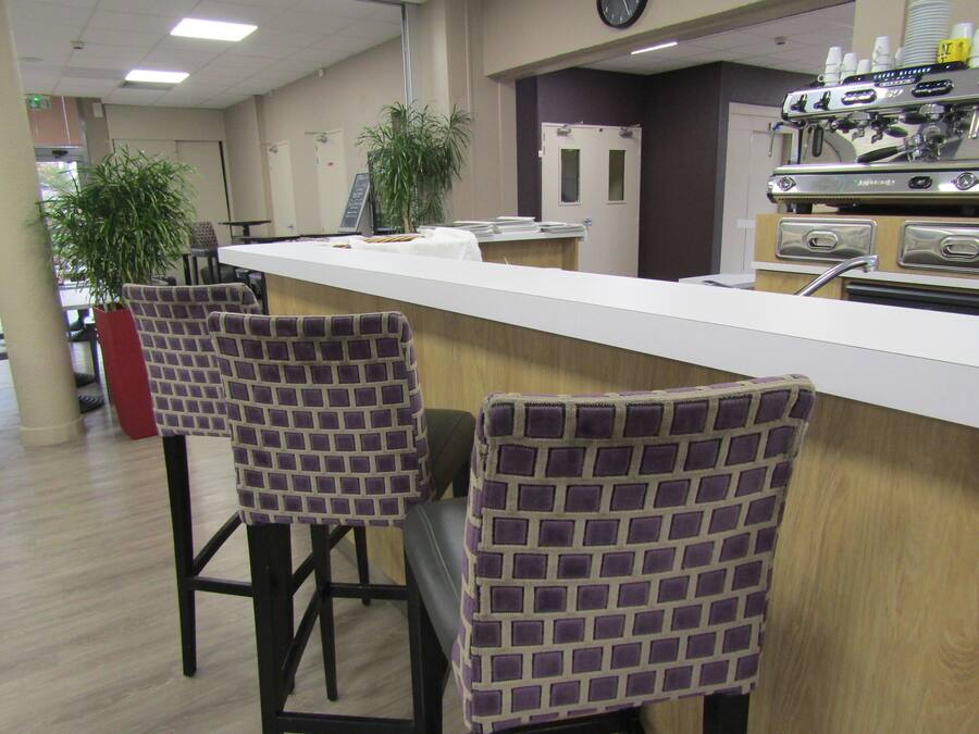 Een bar met twee gestreepte stoelen, een toonbank en een koffieapparaat.