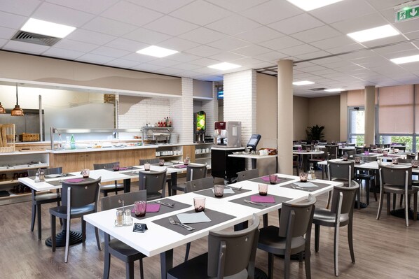 A spacious cafeteria with multiple tables and chairs, equipped with water dispensers and a coffee machine.