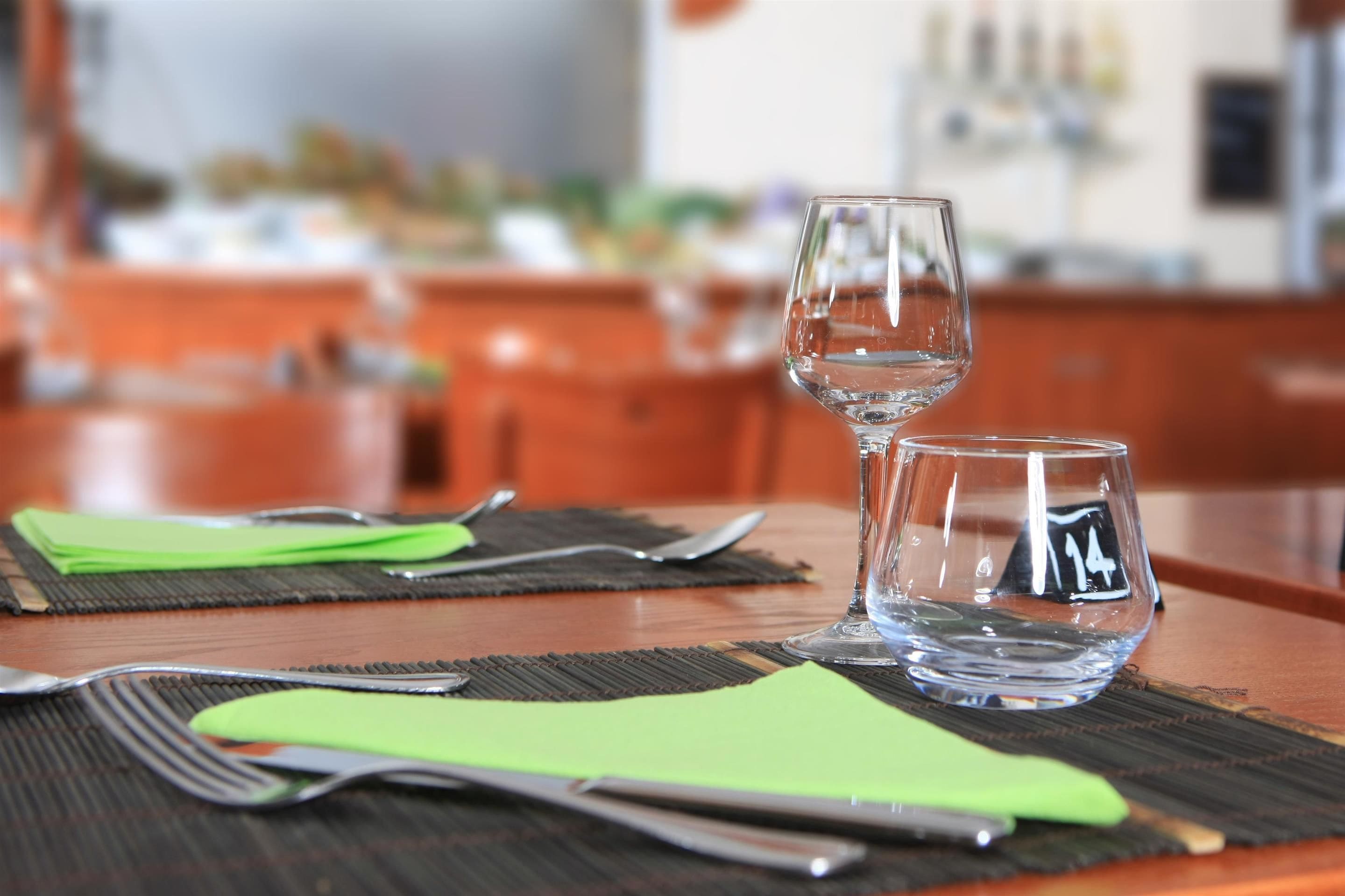 Une table à manger avec un ensemble de couverts et deux verres, sur un fond flou qui évoque un restaurant ou un espace de restauration.