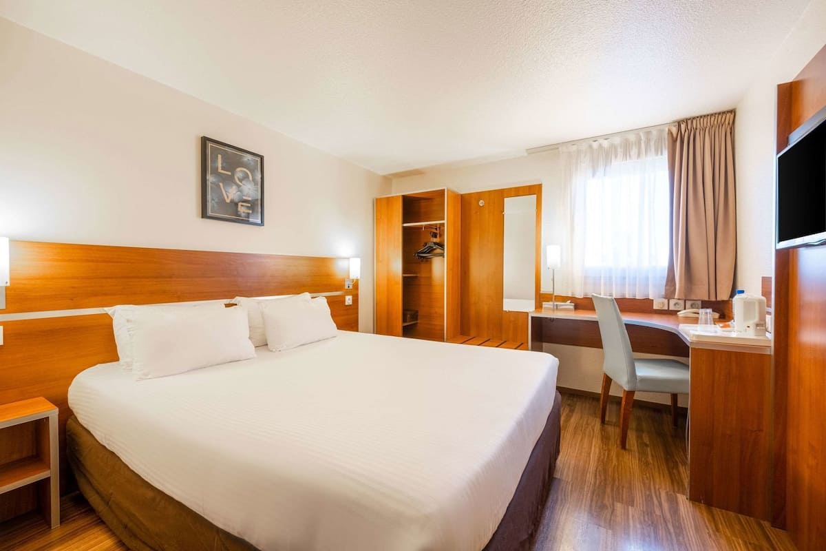 Habitación de hotel con una cama grande, un escritorio, una silla, un armario y un televisor.