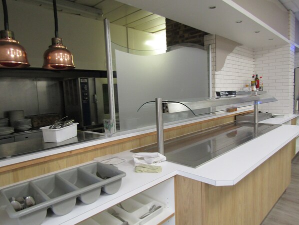 Una cocina moderna con electrodomésticos de acero inoxidable, un separador de vidrio y lámparas colgantes de cobre.