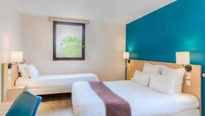 A hotel room with two beds, a desk, and a window with a view of greenery.