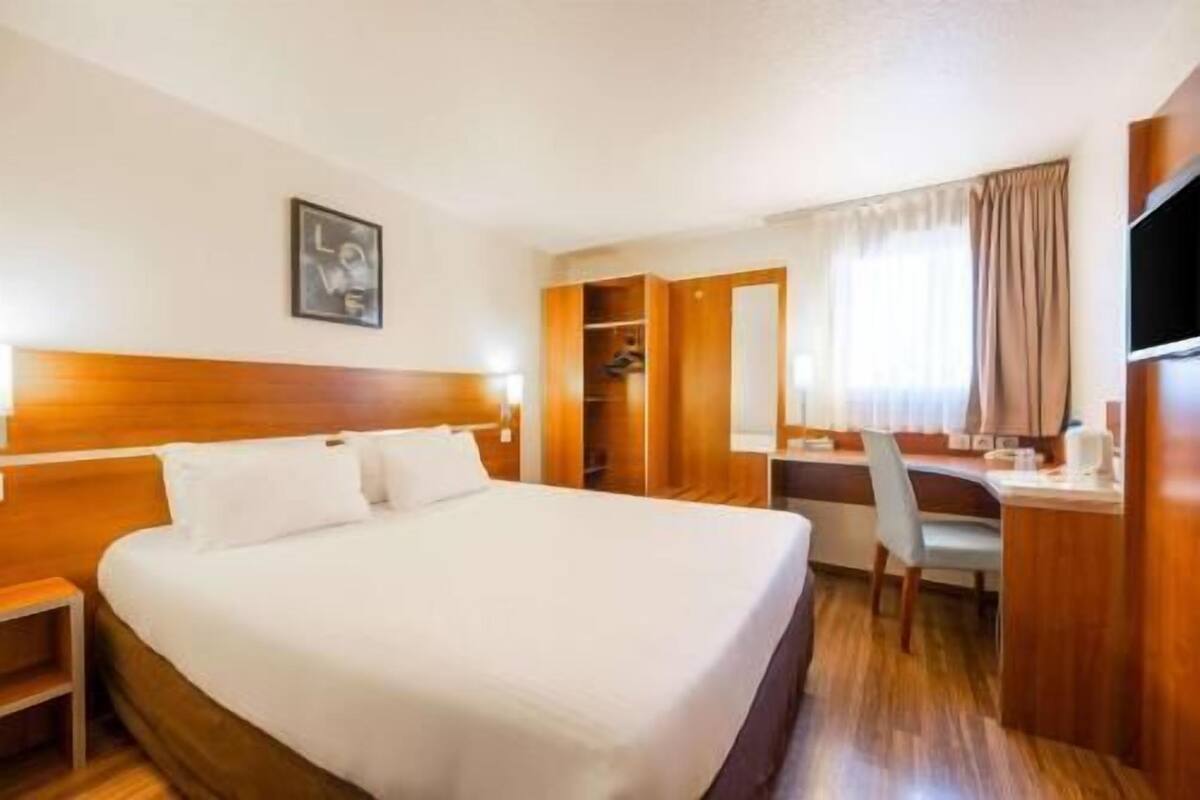 Una habitación de hotel con cama, escritorio, silla, armario y televisión.