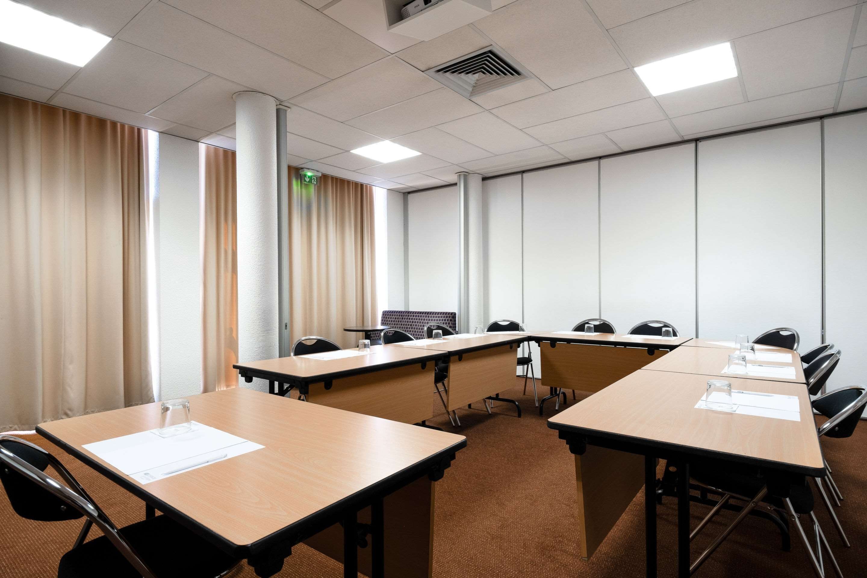 Un salón de conferencias con mesas largas, sillas y un amplio ventanal con cortinas.