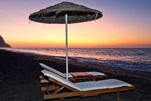 Sulla spiaggia, sabbia scura, lettini da mare, ombrelloni