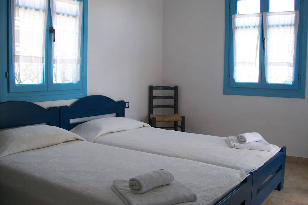 A room with two single beds, a chair, and two windows with curtains.