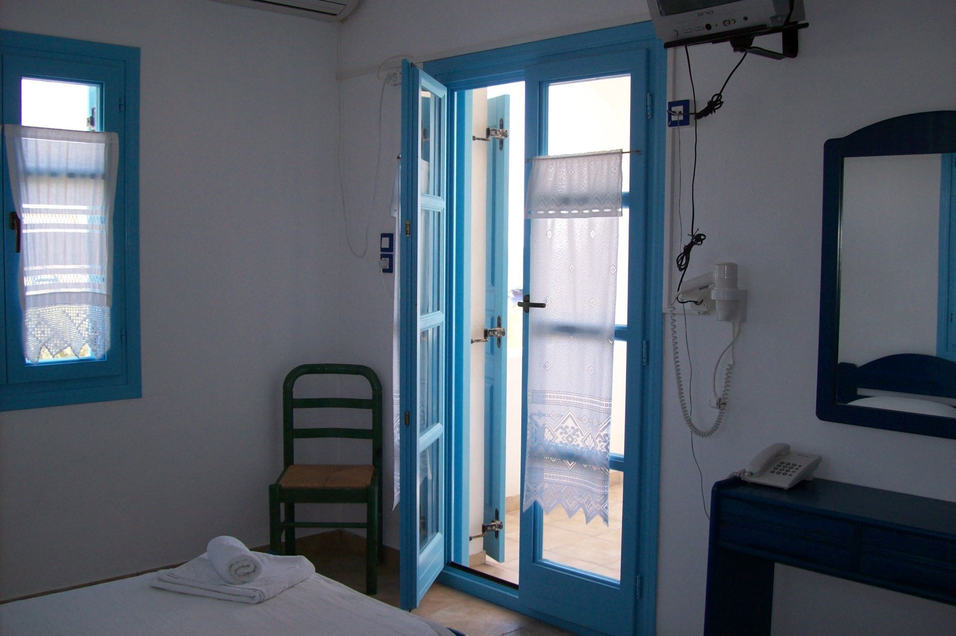 A room with a bed, a chair, a bathroom with a mirror, and a telephone.