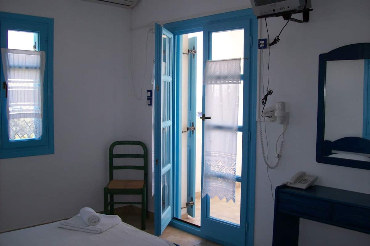 A room with a bed, a chair, a bathroom with a mirror, and a telephone.
