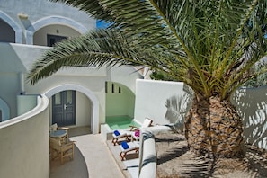 A sunlit courtyard with a palm tree, a pool, and lounge chairs. - Atlantis Beach Villa (Santorini)