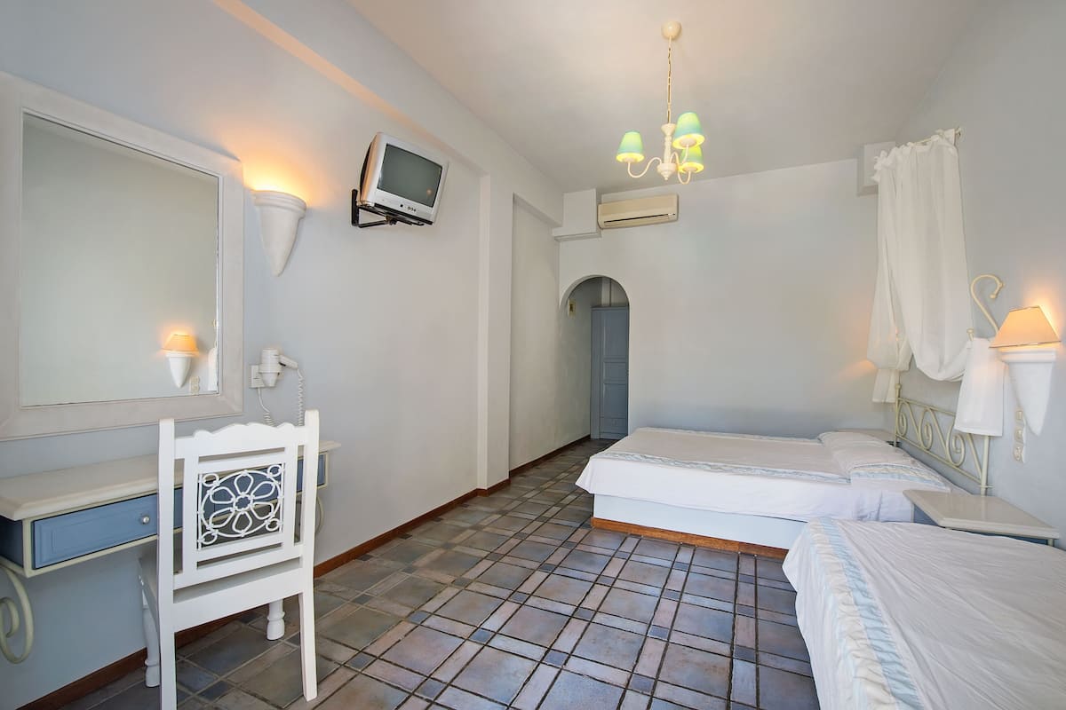 A bedroom with two beds, a desk, a chair, a TV, and a chandelier.