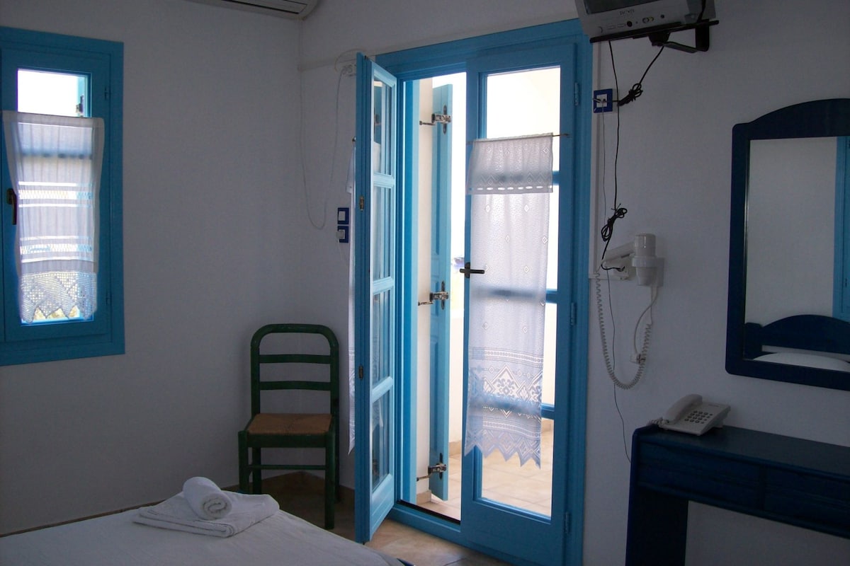 A room with a bed, a chair, a bathroom with a mirror, and a telephone.