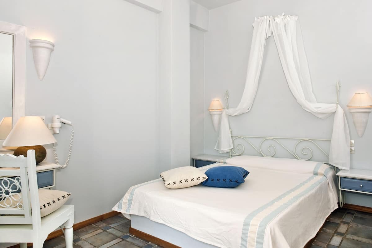 A bedroom with a bed, bedside lamps, a chair, a mirror, and a canopy bed.