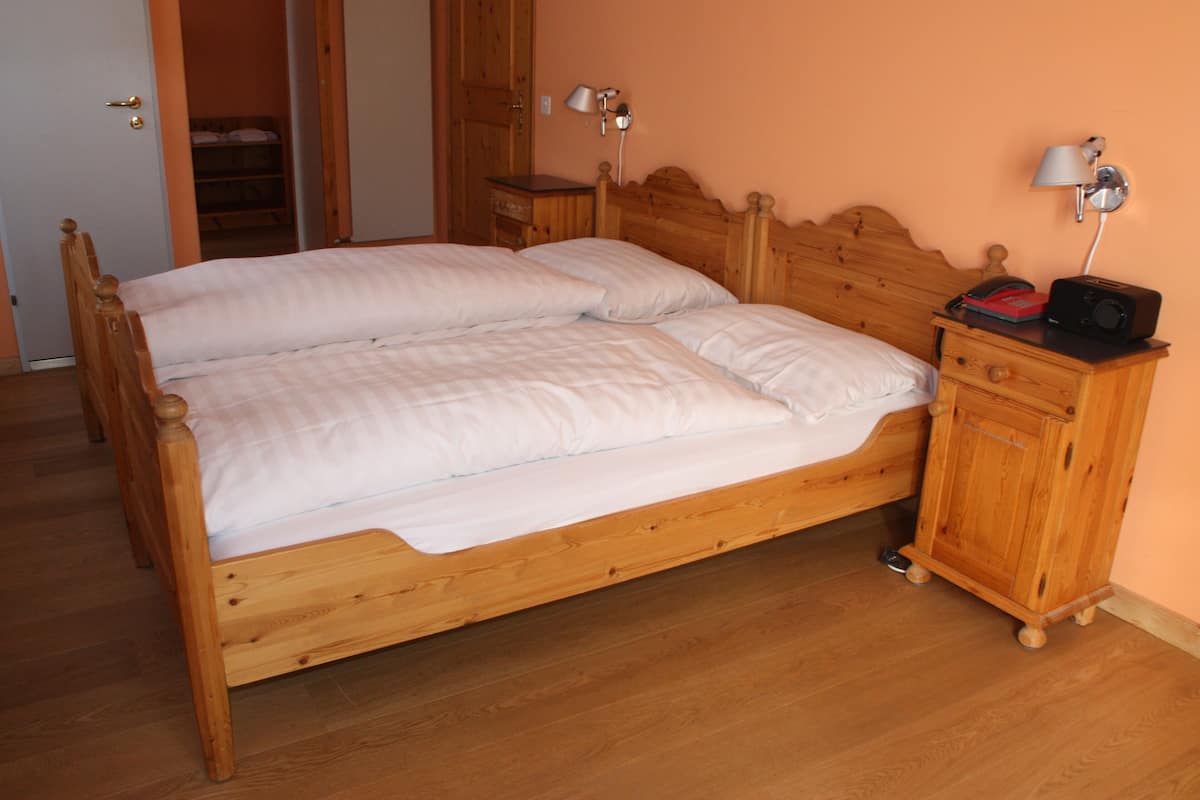 A double wooden bed with white bedding, a wooden nightstand with a radio, and a door leading to a closet.