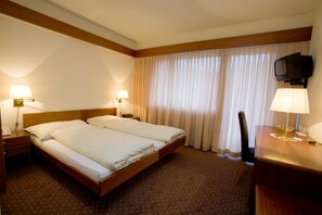 A hotel room with a double bed, two bedside tables with lamps, a TV mounted on the wall, and a desk with a chair. - Hotel Danilo-Pianta (Surses)