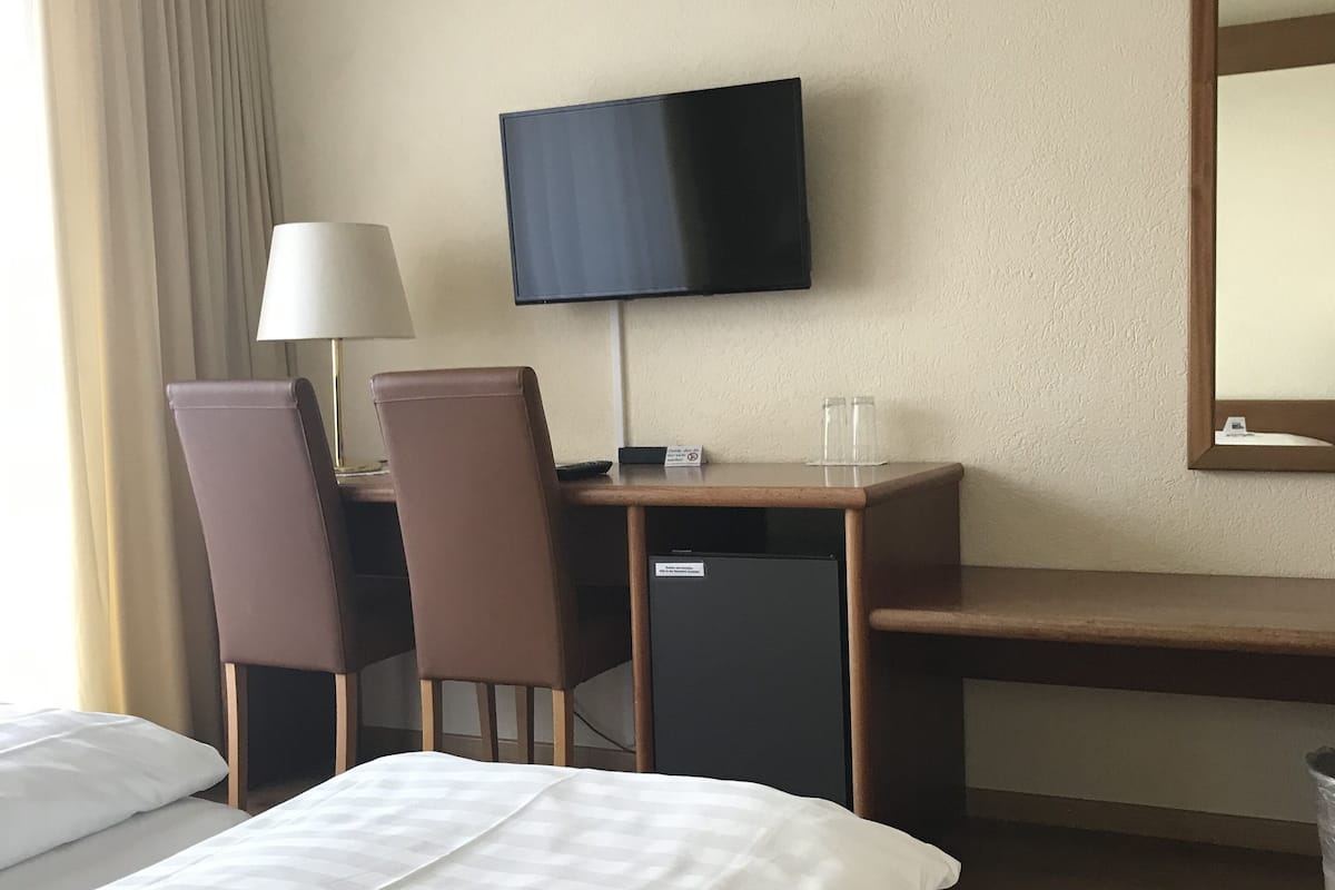A hotel room with a bed, a desk with a computer, a television, and two chairs.