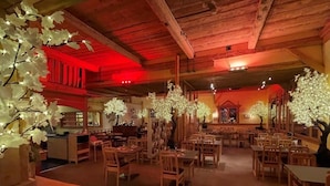 A restaurant with wooden tables and chairs, red lighting, and decorative trees with lights.