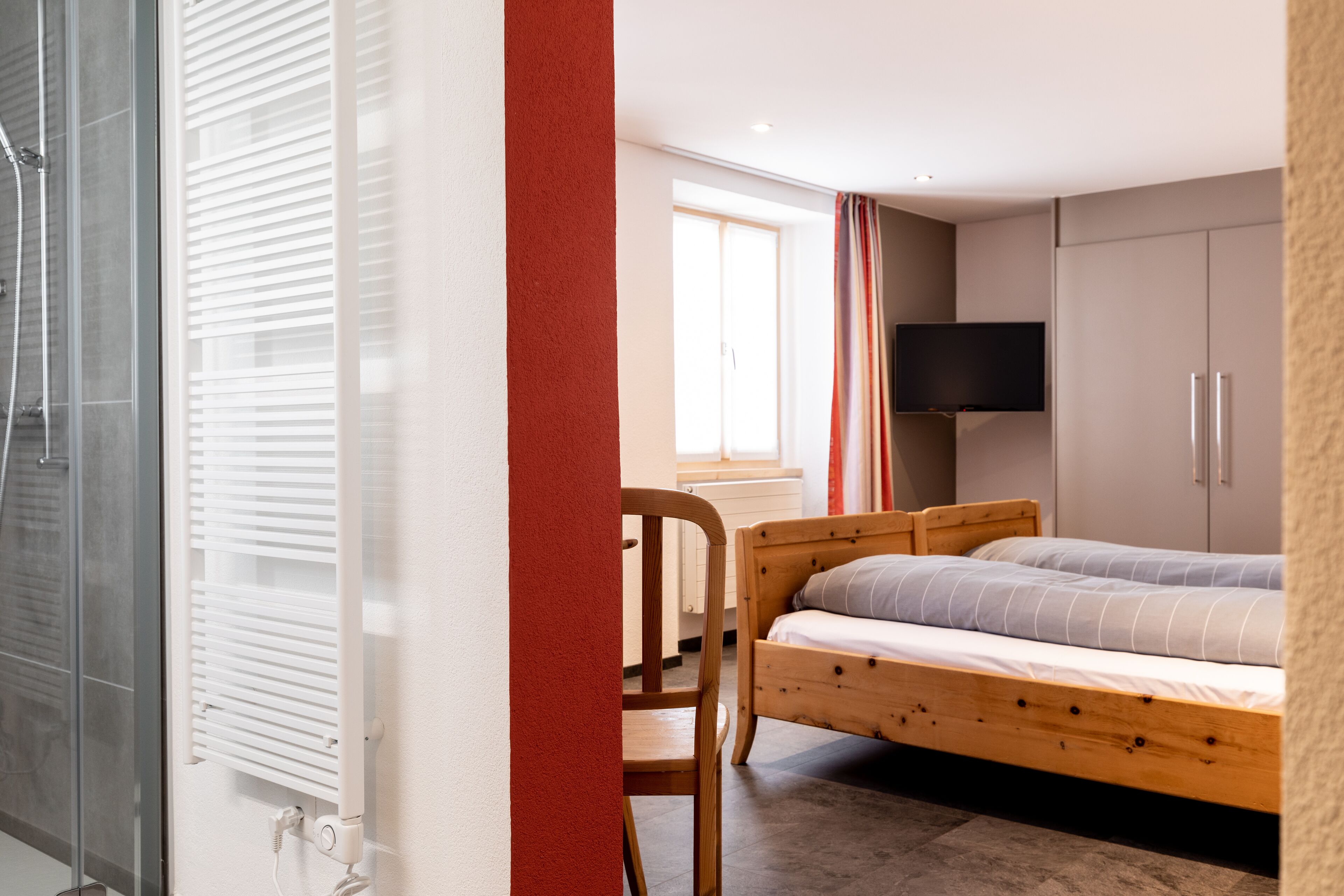 A bedroom with a bed, a chair, a TV, and a window.