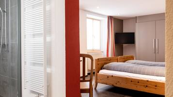 A bedroom with a bed, a chair, a TV, and a window.